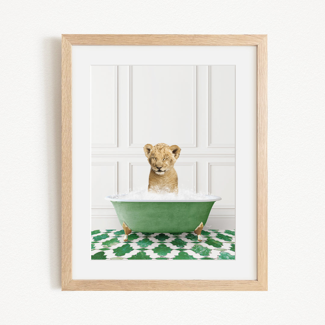 A young lion cub is sitting in a green bathtub filled with water, surrounded by a green and white patterned rug.