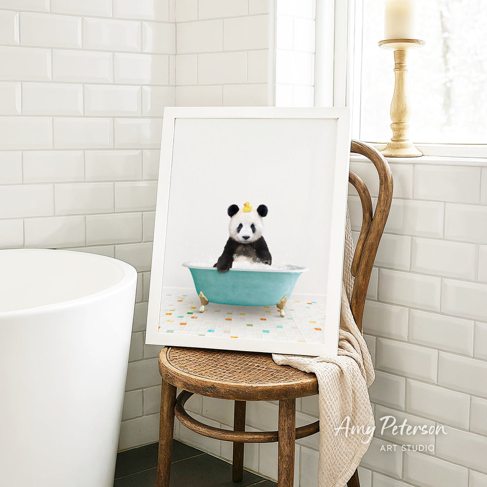 A framed image of a panda bear sitting in a bathtub, with a towel draped over the back of a chair in a bathroom setting.