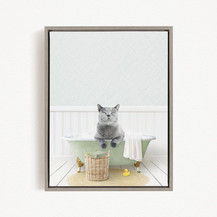 A gray cat sitting in a green bathtub, with a basket of toys and a yellow rubber duck nearby.