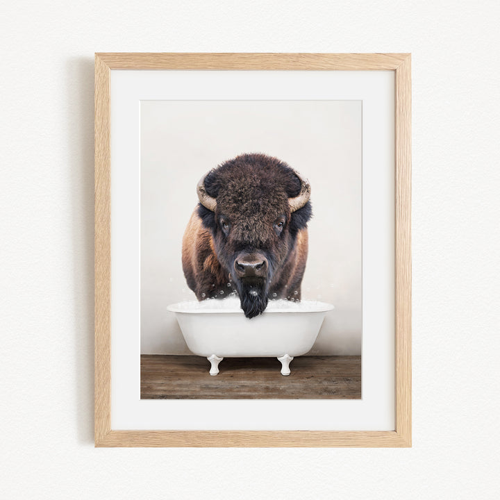 A buffalo with large horns is standing in a white bathtub, with its head submerged in the water.