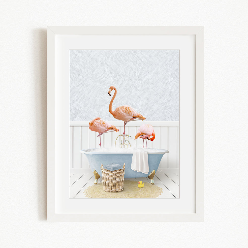 A framed image depicting three flamingos standing in a bathtub filled with water, surrounded by various bathroom items such as a basket, a towel, and a yellow rubber duck.