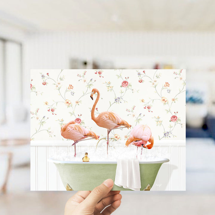 A hand holds up a collage of three images featuring pink flamingos in a bathtub, with a floral wallpaper backdrop.