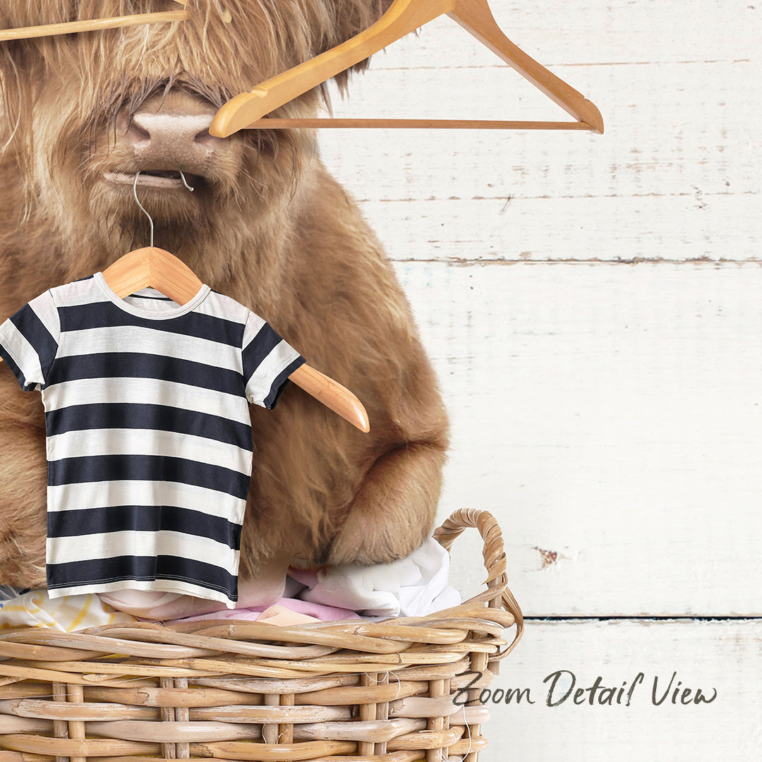 A large, furry animal, possibly a yak or a similar creature, is sitting inside a wicker basket filled with clothing items, including a striped shirt.