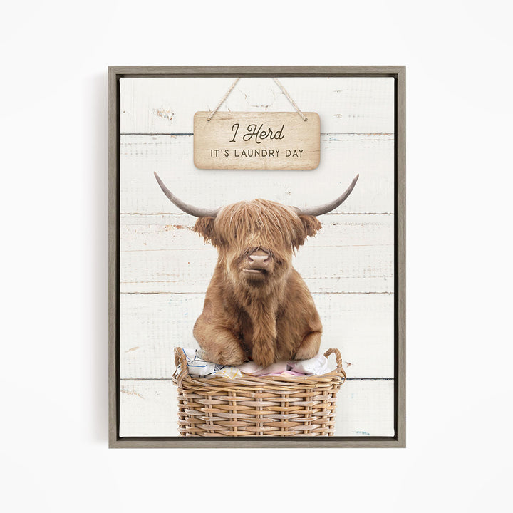 A framed image of a Highland cow sitting in a wicker basket, with a sign above it that says "It's laundry day".