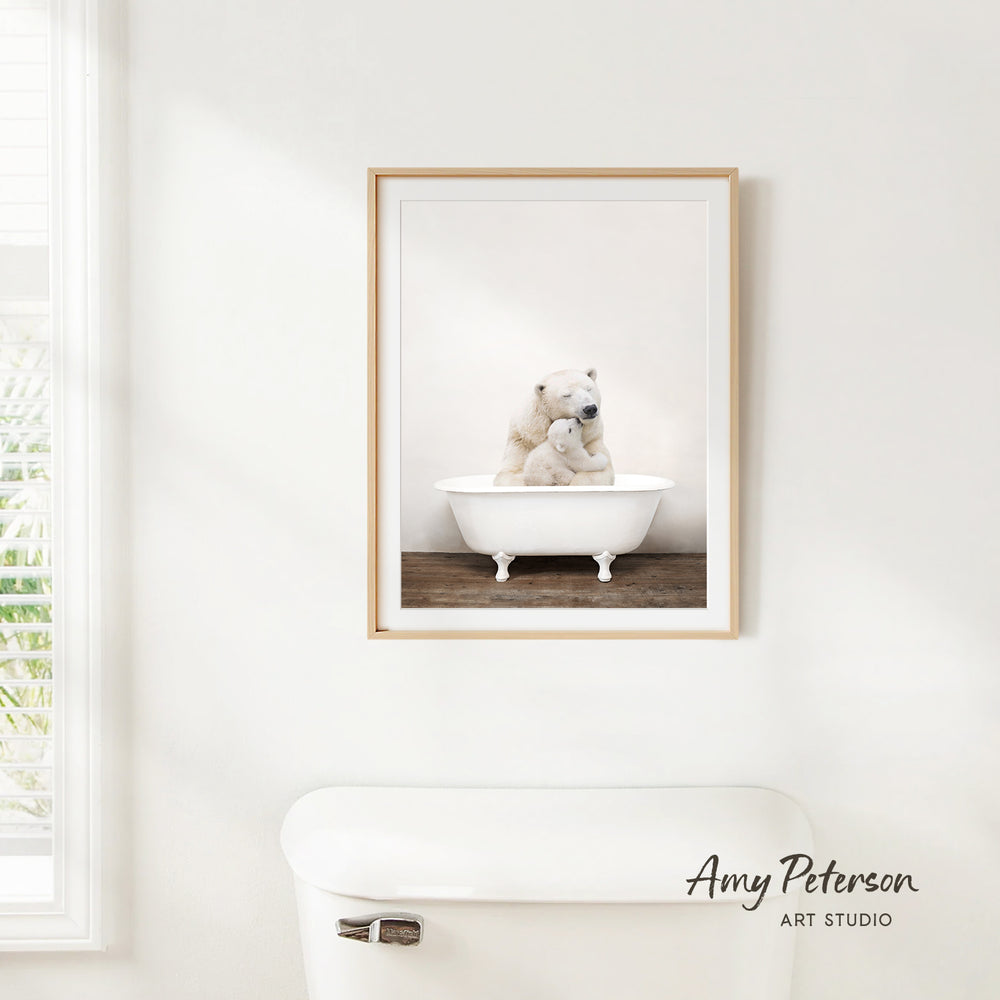 A framed photograph of two polar bears sitting in a white bathtub is hanging on a white wall.