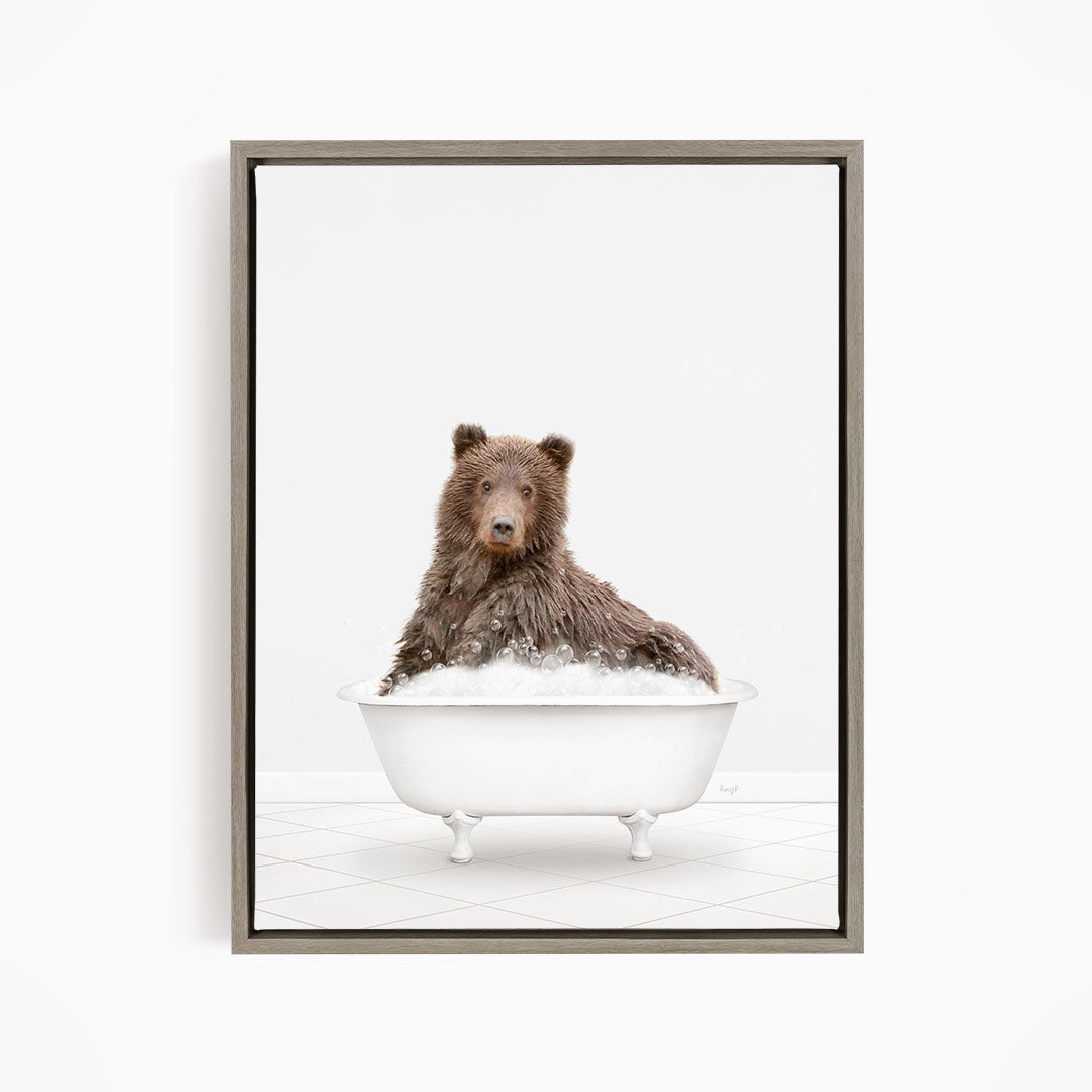 A brown bear sitting in a white bathtub filled with bubbles, looking directly at the camera.
