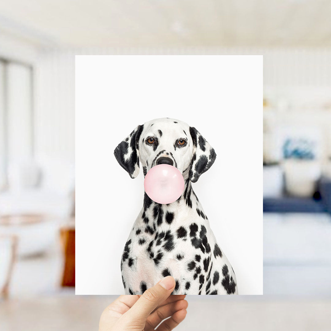 A Dalmatian dog is holding a pink bubble gum bubble in its mouth, with a blurred background suggesting an indoor setting.
