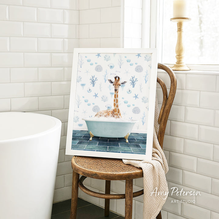 A framed image of a giraffe sitting in a bathtub, surrounded by blue and white floral patterns, is displayed on a wooden chair in a bathroom setting.