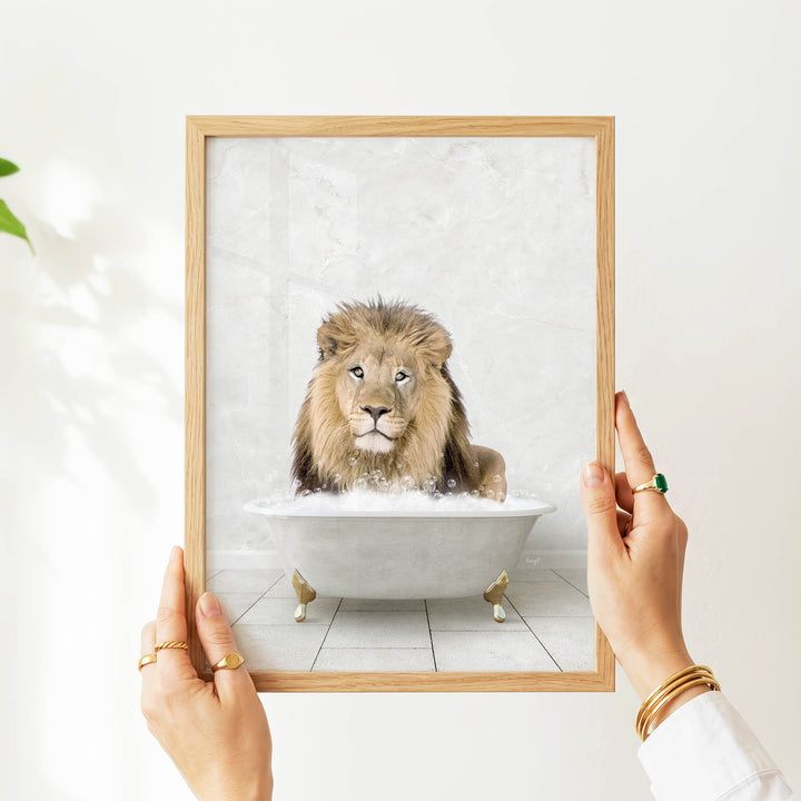 A person's hands are holding a framed picture of a lion sitting in a bathtub filled with bubbles.