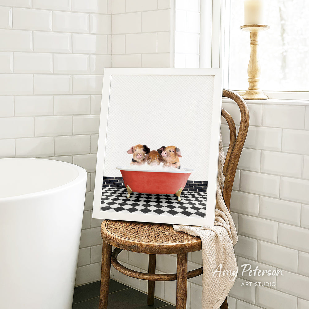 A framed image of two small dogs sitting in a red bathtub, surrounded by a black and white checkered floor, is displayed on a wooden chair in a bathroom setting.