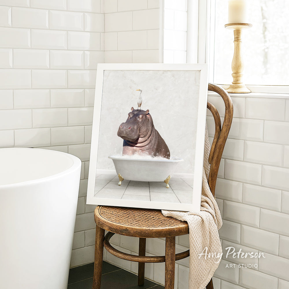 A framed image of a hippopotamus sitting in a bathtub is displayed on a wooden chair in a bathroom setting.