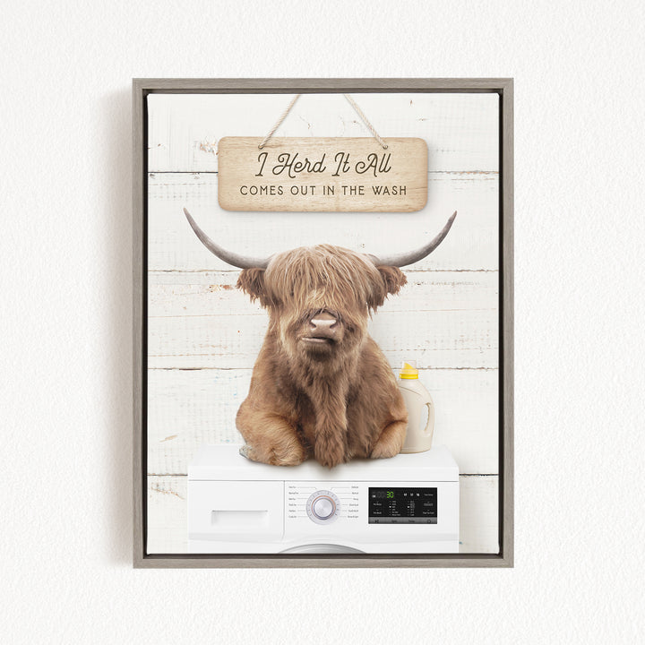A framed image depicting a Highland cow with long horns sitting on a white washing machine, with a sign above that reads "I Herd It All Comes Out in the Wash".