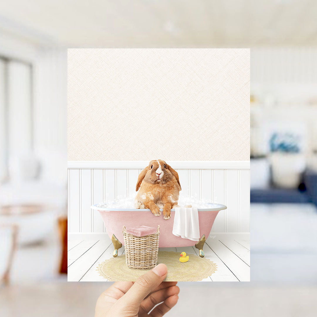 A brown rabbit sitting in a pink bathtub filled with bubbles, surrounded by a yellow rubber duck and a white towel.
