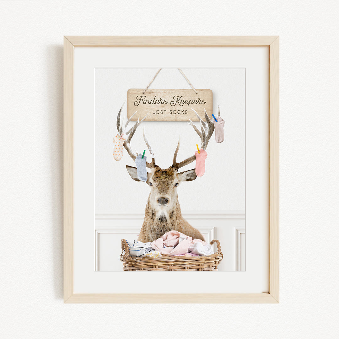 A deer with antlers sits in a basket filled with clothes, with a sign above that reads "Finders Keepers Lost Socks".