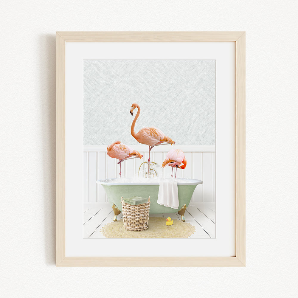 A framed image depicting three flamingos standing in a bathtub, with a basket of bath toys and a yellow rubber duck nearby.