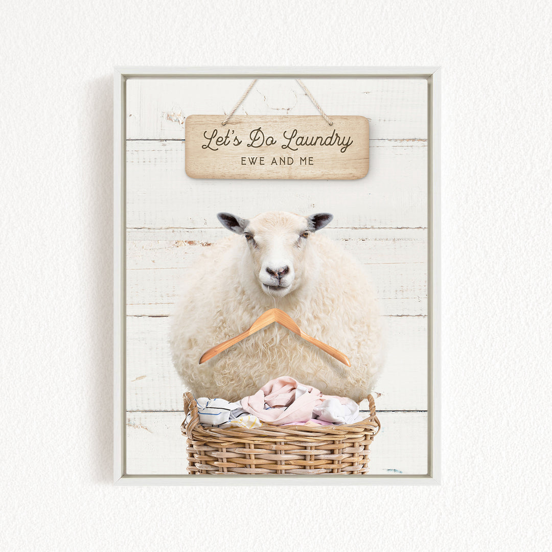 A white sheep sits in a wicker basket filled with laundry, with a wooden sign above that reads "Let's Do Laundry Ewe and Me".