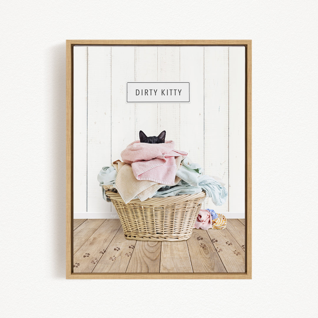 A framed image of a cat sitting in a basket filled with clothes, with the text "Dirty Kitty" displayed above the basket.