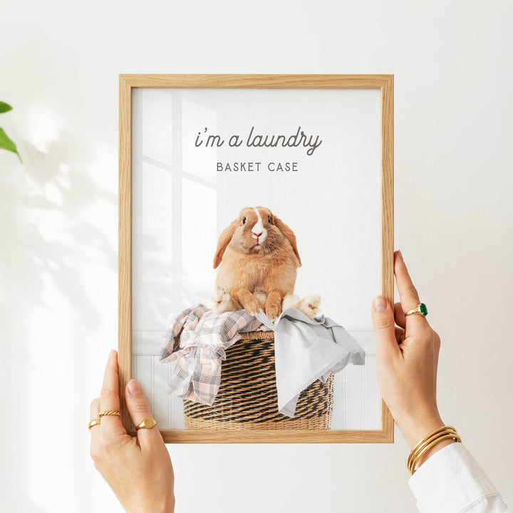 A person's hands are holding a picture frame with a photograph of a rabbit sitting in a basket.