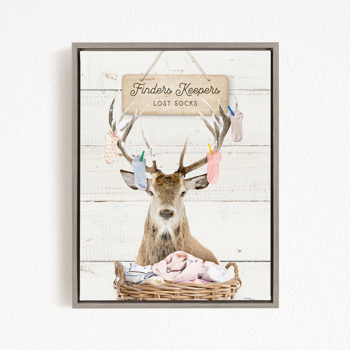 A deer with antlers is sitting in a basket filled with socks, with a sign above that says "Finders Keepers Lost Socks".