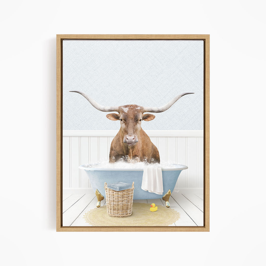 A brown bull with long horns is sitting in a blue bathtub filled with bubbles, surrounded by a basket of rubber ducks and a towel.