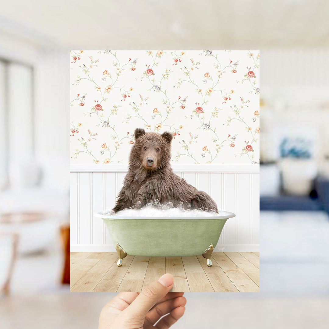 A brown bear sitting in a green bathtub filled with bubbles, with a floral patterned wall behind it.