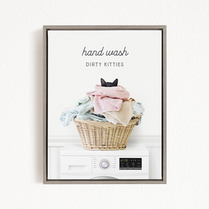 A framed image depicting a cat sitting in a basket filled with laundry, with the text "hand wash dirty kitties" written above the basket.
