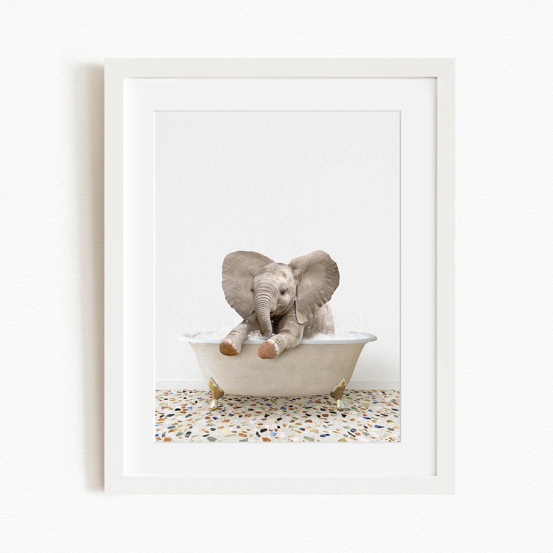 A baby elephant sitting in a white bathtub, with its trunk raised and ears flapping, against a white background.