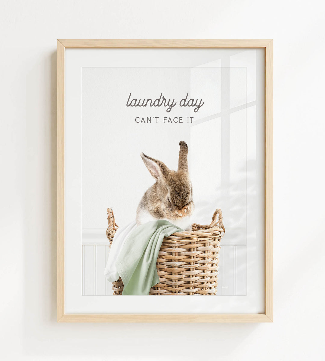 A framed image of a rabbit sitting in a wicker basket, with the text "laundry day can't face it" written above the rabbit.