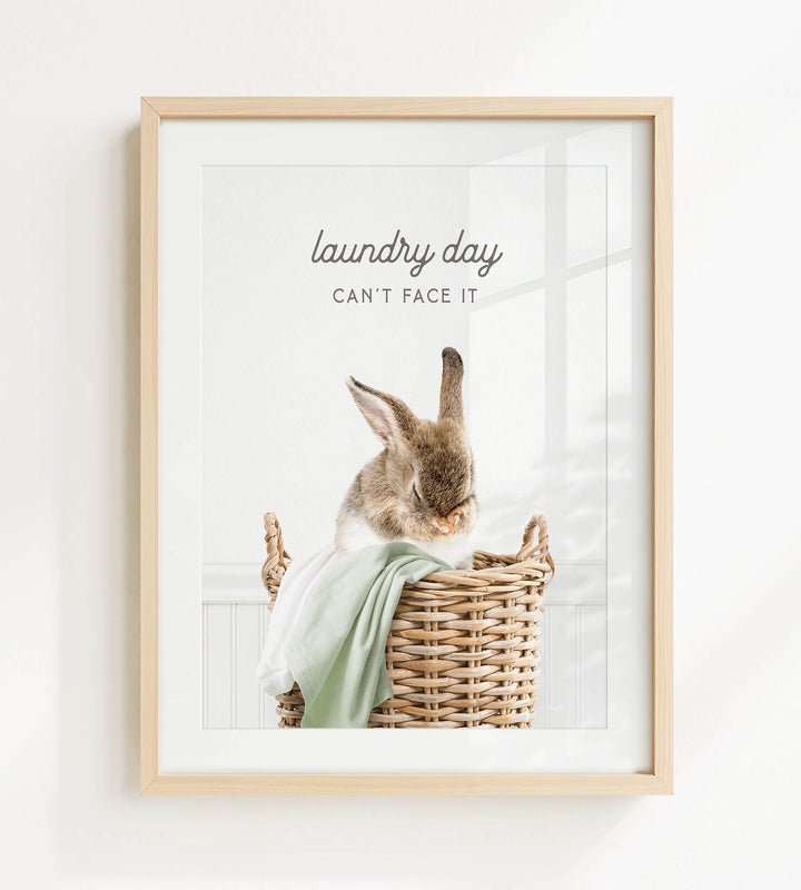 A framed image of a rabbit sitting in a wicker basket, with the text "laundry day can't face it" written above the rabbit.