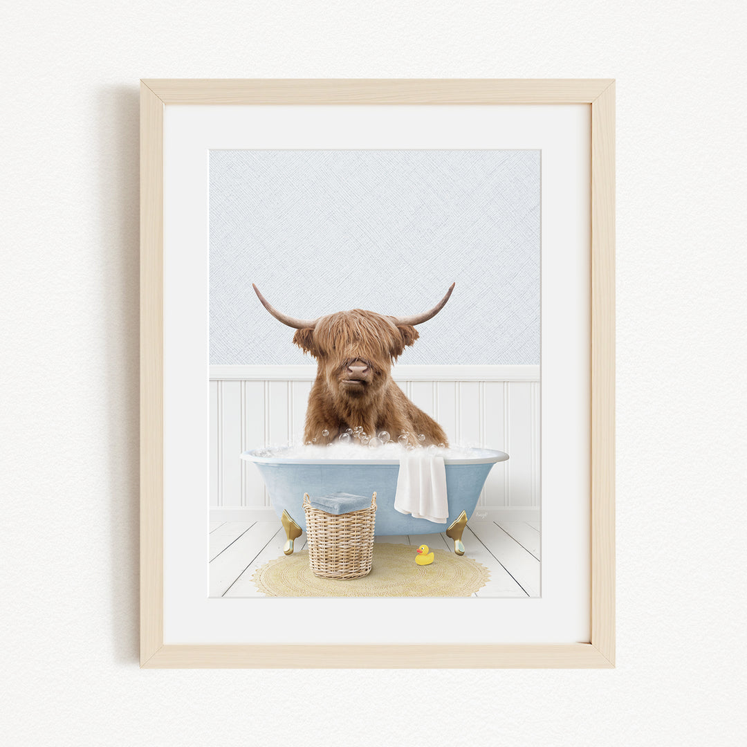 A brown cow with long horns is sitting in a blue bathtub, surrounded by a yellow rubber duck and a basket.