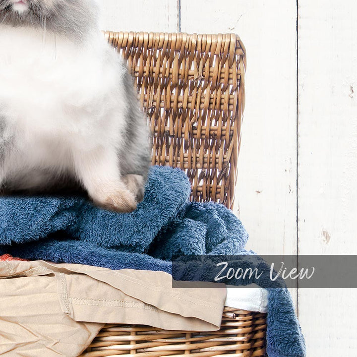 A fluffy gray and white cat sitting on a blue towel in a wicker basket.