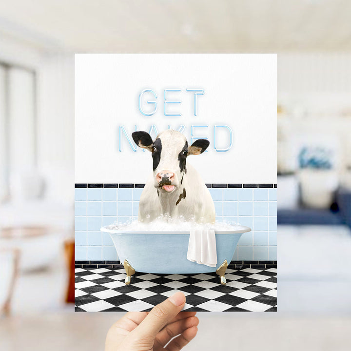 A hand holding a framed image of a cow sitting in a bathtub with the text "GET NAKED" displayed above it.