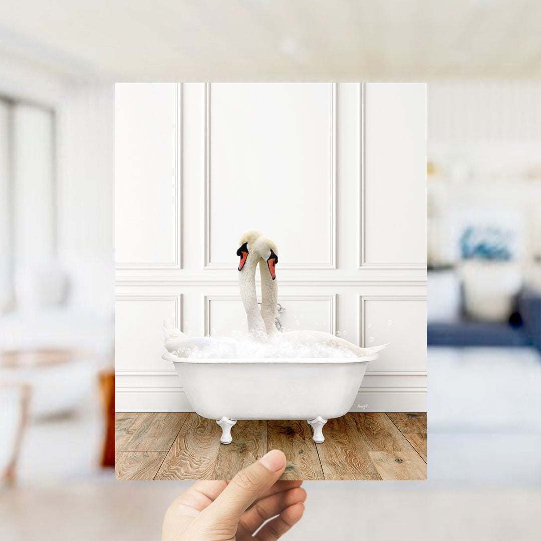 A hand holds up a photograph of a white swan sitting in a bathtub filled with bubbles, with a blurred background suggesting a bathroom setting.