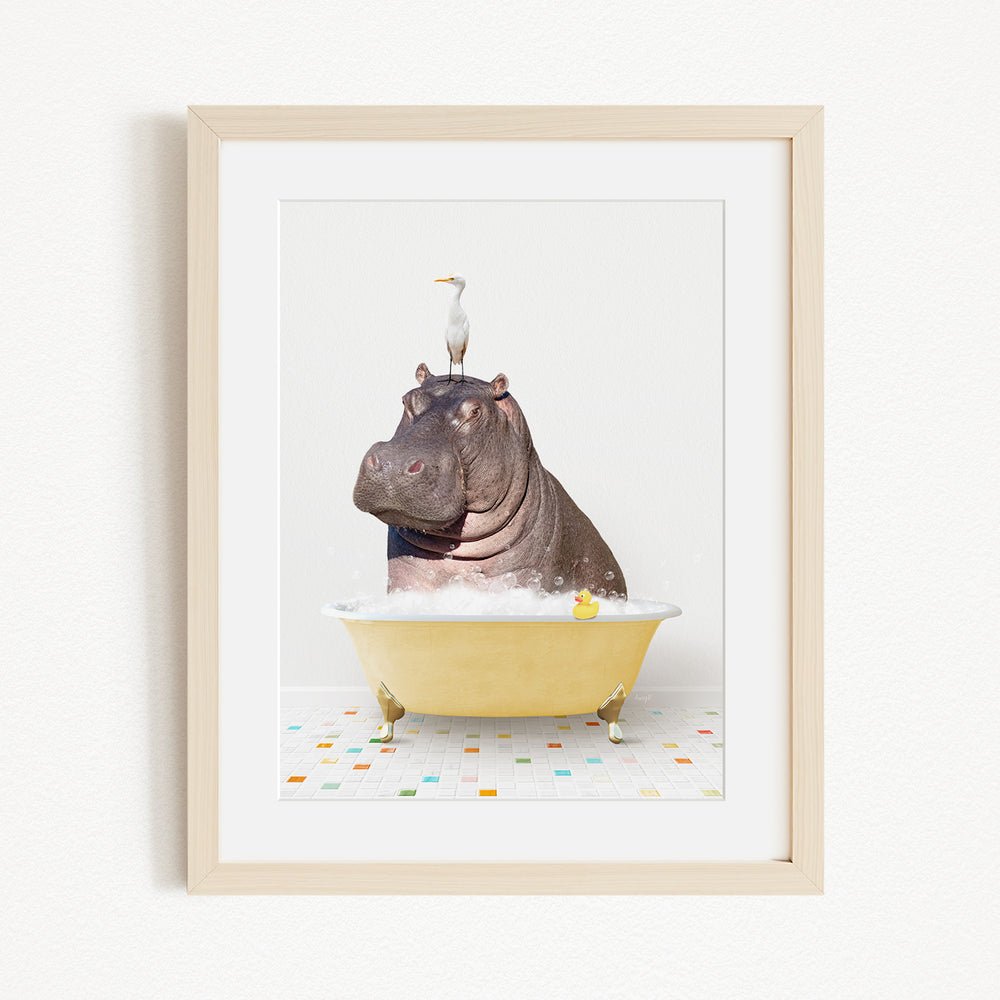 A framed image depicting a hippopotamus sitting in a yellow bathtub, with a bird perched on its head.