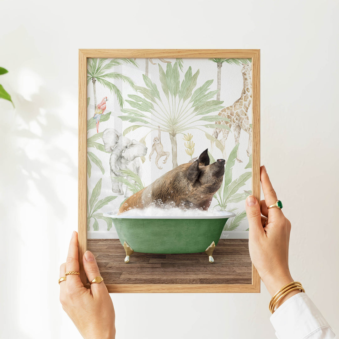 A person's hands are holding a framed picture of a pig sitting in a green bathtub, surrounded by tropical foliage and animals.