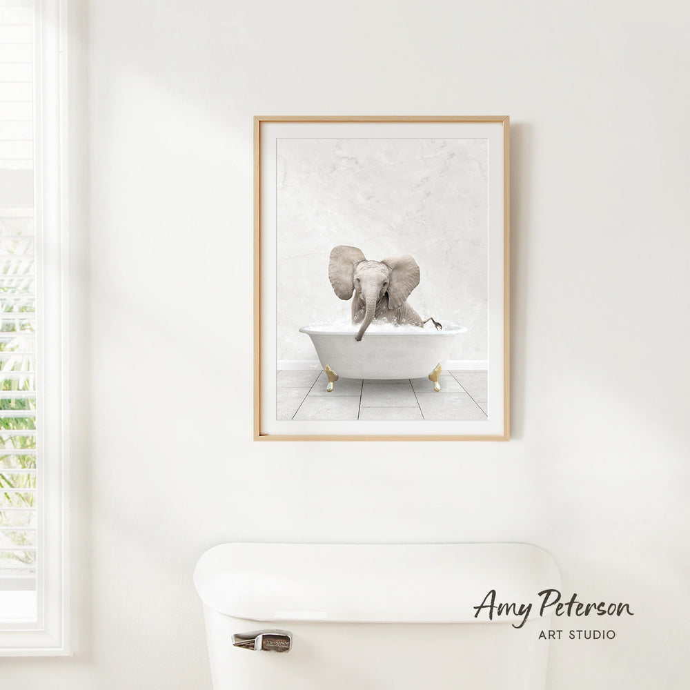 A framed image of an elephant sitting in a bathtub is hanging on a white wall.