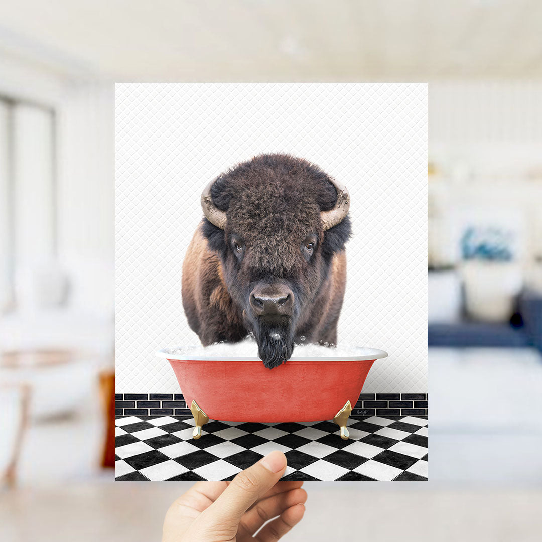 A buffalo with horns is standing in a red bathtub, with a hand holding up the image to show it.