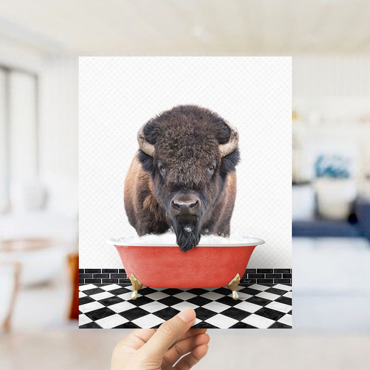 A buffalo with horns is standing in a red bathtub, with a hand holding up the image to show it.