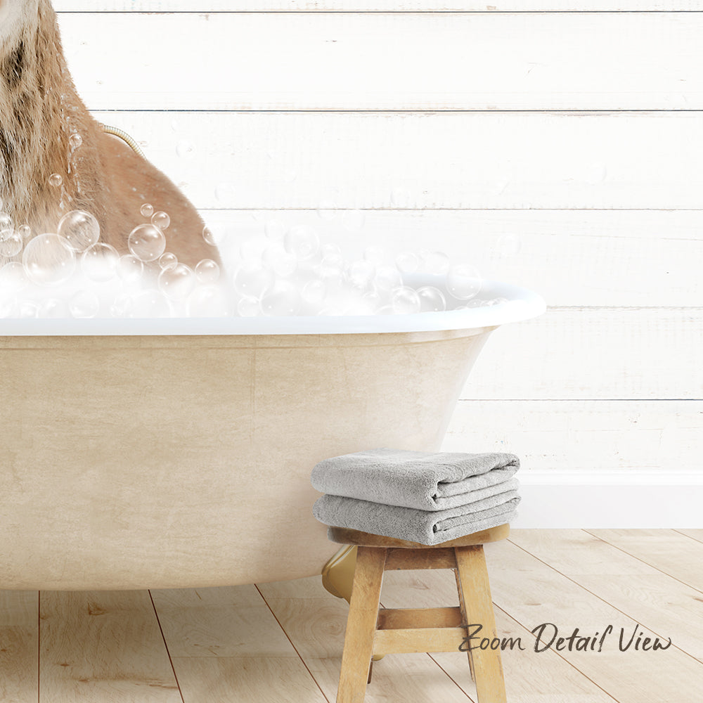 A dog is taking a bath in a white bathtub, surrounded by bubbles, with a towel and stool nearby.