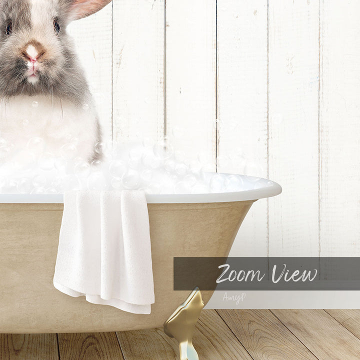 A fluffy white rabbit sitting in a bathtub filled with bubbles, with a towel draped over the side and a "Zoom View" label below the image.