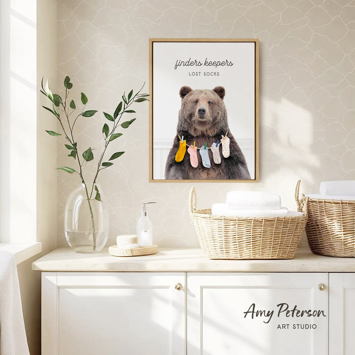 a framed poster of a bear wearing socks, hanging on a wall above a white cabinet with baskets.