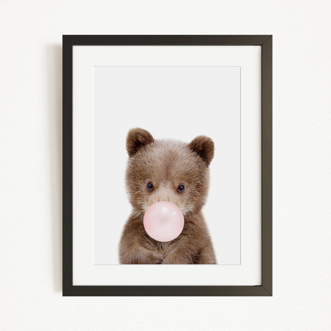 A cute brown bear is blowing a bubble with a pink bubble gum bubble.