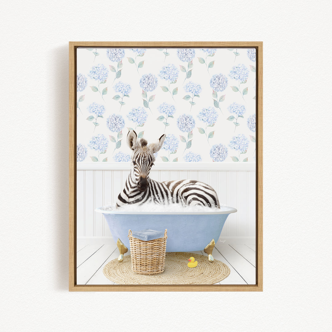 A zebra is sitting in a blue bathtub filled with water, surrounded by a wicker basket and two rubber duckies.