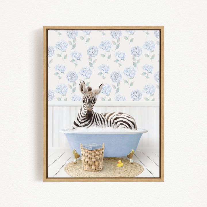 A zebra is sitting in a blue bathtub filled with water, surrounded by a wicker basket and two rubber duckies.