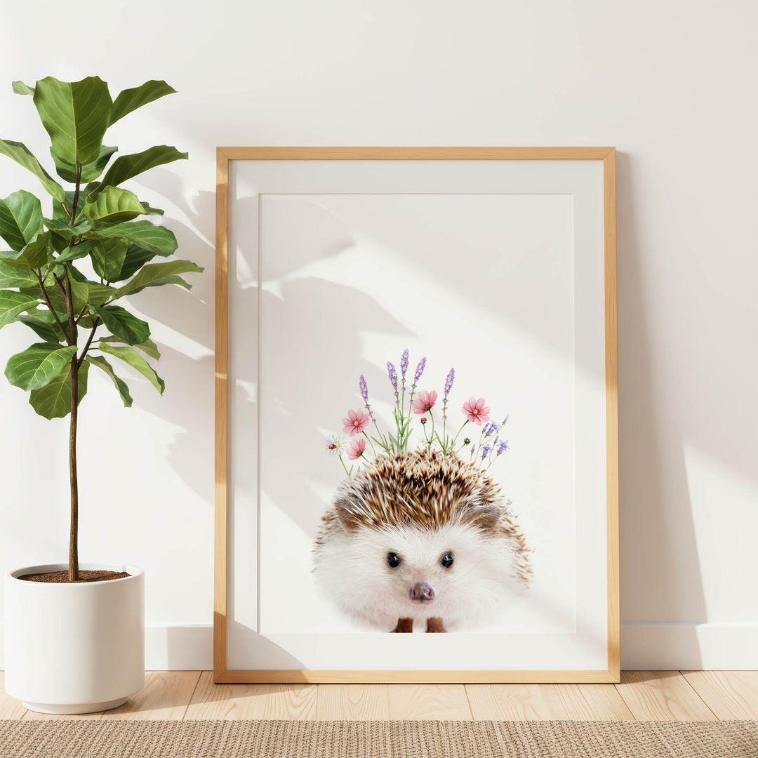 a framed picture of a hedgehog with flowers on its head, placed on a wooden floor next to a potted plant.