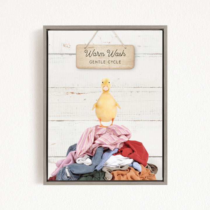 A yellow duck standing on a pile of clothes, with a wooden sign above that reads "Warm Wash Gentle Cycle".