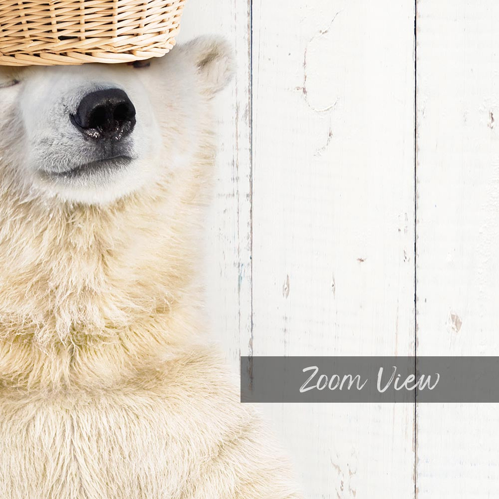 A close-up of a polar bear's face peeking out from behind a woven basket, with a white wooden background.