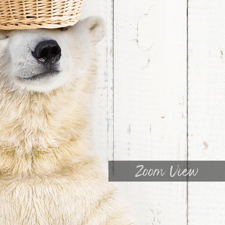 A close-up of a polar bear's face peeking out from behind a woven basket, with a white wooden background.