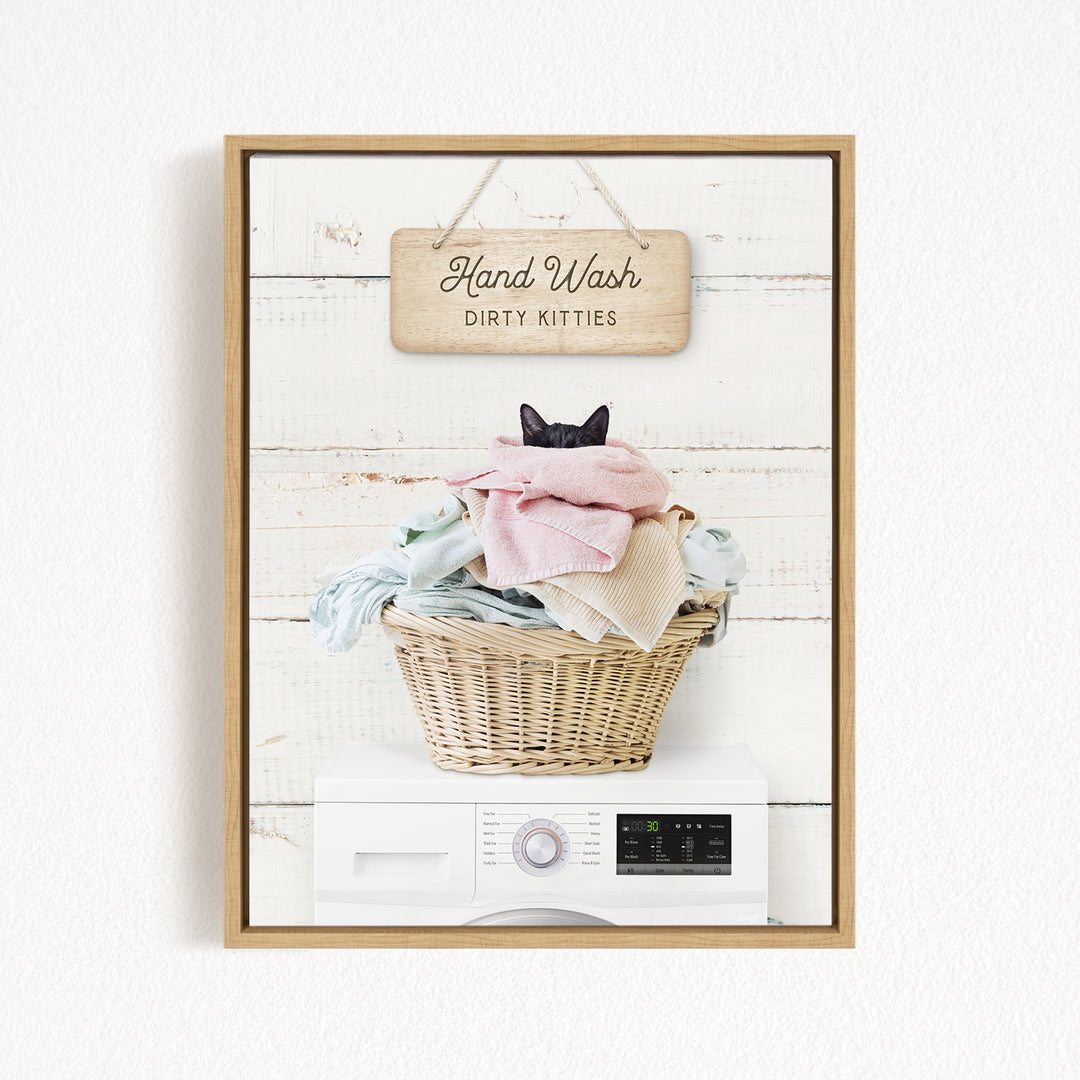 A framed image of a cat sitting in a basket filled with laundry, with a sign above that says "Hand Wash Dirty Kittens".