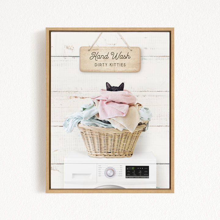 A framed image of a cat sitting in a basket filled with laundry, with a sign above that says "Hand Wash Dirty Kittens".